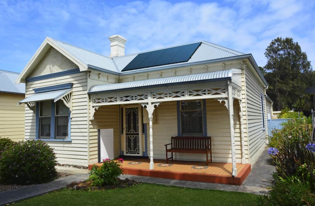 Image of a traditional Australian house with solar panels on the roof and a Tesla battery in the front porch.